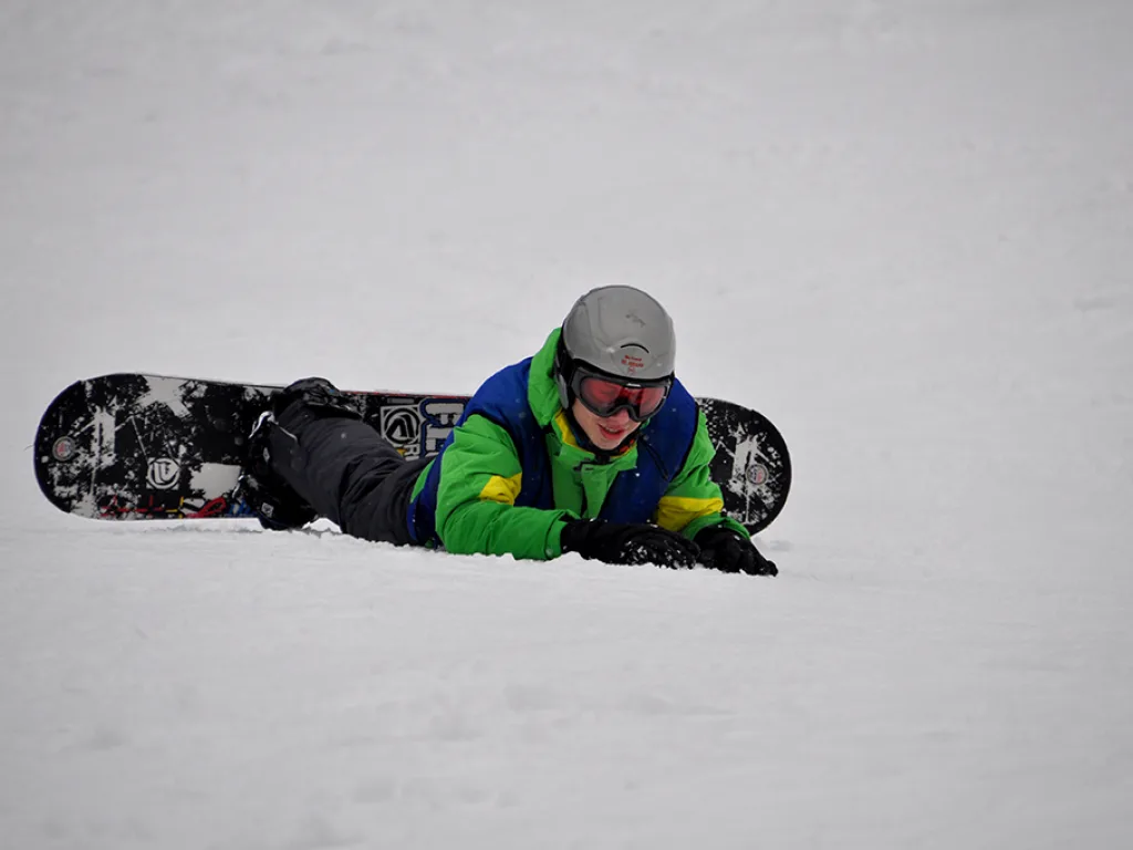 Snowboarder liegt lachend im Schnee.